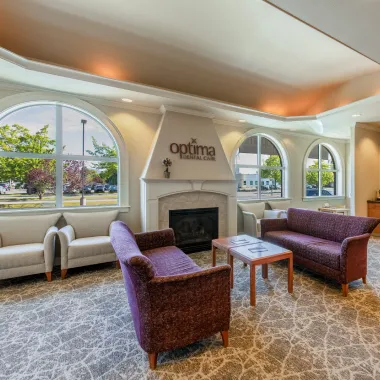 Reception area with a curved counter, two chairs for patients, warm lighting, and a back office space with storage cabinets and potted plants.