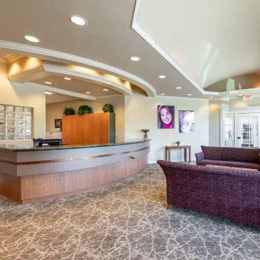 Wide view of the waiting area at Optima Dental Care, showing multiple seating options, a fireplace centerpiece, and large windows creating a bright and welcoming space.